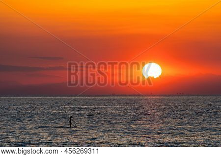 Lonely Person Riding Paddling A Sup Into A Spectacular Sunset.