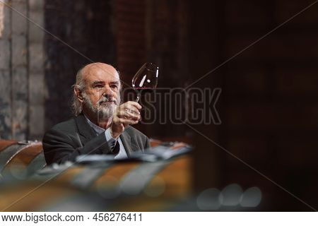 Senior Caucasian Tourist, Greybeard Elegant Man Tasting Red Wine In An Underground Wine Cellar Of Th