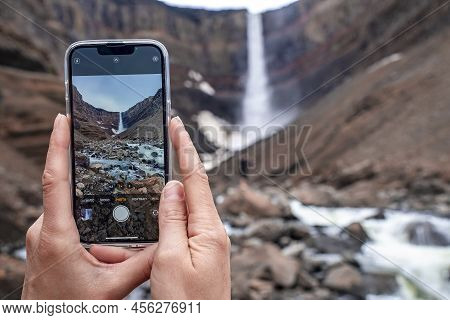Cropped Image Of Tourist Traveler Photographing Hengifoss Waterfall On Cellphone
