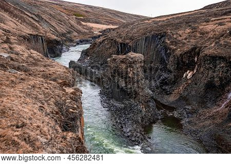 Stream Flowing Amidst Basalt Columns Rock Formation At Eastfjords Against Sky