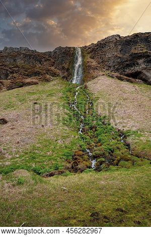 Scenic Gljufrabui Waterfall Flowing From Mountain Against Cloudy Sky At Sunset