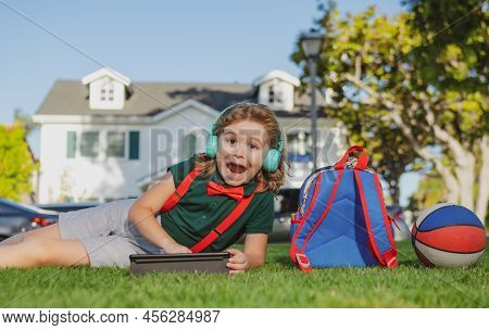 Kid With Tablet Device Sitting Outdoor In Garden, Wearing Short And Shirt. Lttle Child Outdoor Schoo