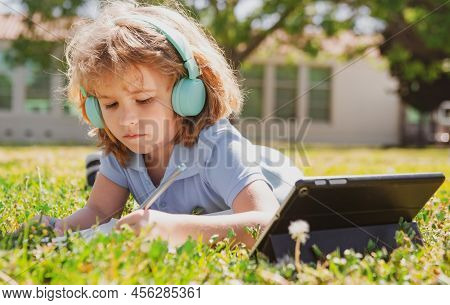 Child Homework Outside In Scholl Yard. Little Schoolboy Pupil With Tablet In The Park On Grass. Self