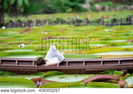 Asian Girl Is Lying Down On The New Vintage Wood Boat On The Lily Lotus Leaf Pond At Outdoor Field.