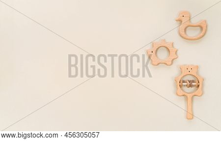 Baby Wooden Teethers And Toys Banner On Pastel Beige Background. Infant Toys And Rattles In Eco Styl