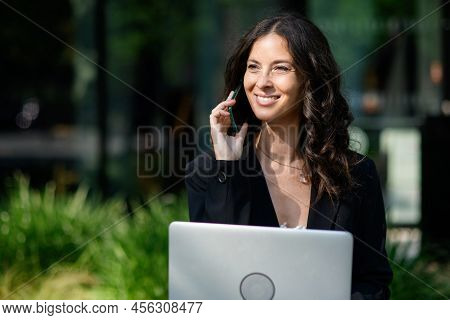 Successful Happy Businesswoman Sitting Using Laptop And Calling On Mobile Outside The Office Bulidin