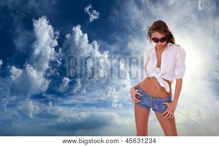 Ung kvinde i jeans shorts stående på blå skyet himmel backgroound