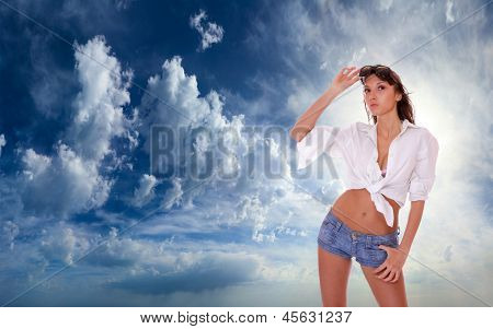 Ung kvinde i jeans shorts stående på blå skyet himmel backgroound