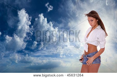 Ung kvinde i jeans shorts stående på blå skyet himmel backgroound