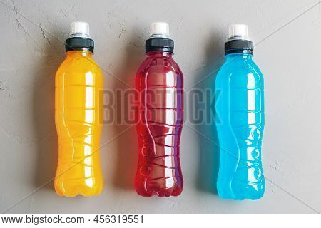 Flat Lay Shot Of Three Bottles Of Orange, Red And Blue Isotonic Drink On A Grey Concrete Background