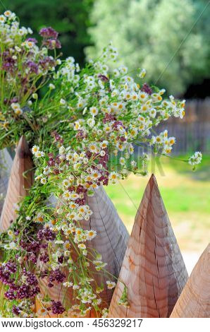 A Wreath Of Wildflowers Hangs On Pointed Wooden Pegs Of The Fence, The Holiday Of The Summer Solstic