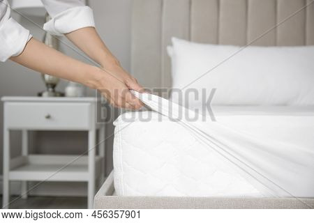 Woman Putting White Fitted Sheet Over Mattress On Bed Indoors, Closeup