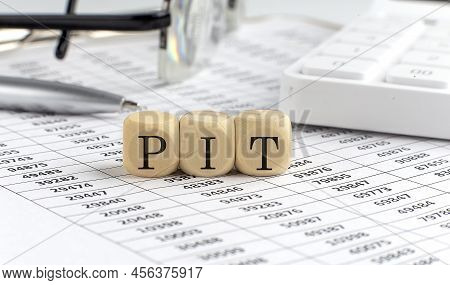 Wooden Cubes With The Word Pit On A Financial Background With Chart, Calculator, Pen And Glasses, Bu