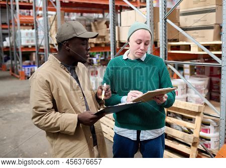 Mature Woman Checking List And Discussing Shipping Together With Her Colleague During Work At Wareho