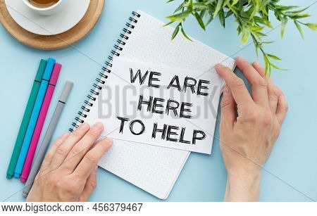 We Are Here To Help. Text On Open Notepad On Blue Background Near White Kup Coffee.