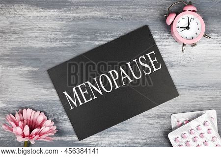 Menopause Word Written On Black Board, Flowers, Clock And Pills On Wooden Background. Women Health A