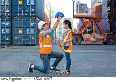 Father And Little Daughter Wearing A Safety Helmet At Container Cargo Site. Business Heir Concept. H