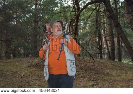 Portrait Of Severe Senior Ukrainian Ranger With Two Rifles Standing In Dark Pine Forest With Readine