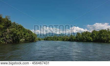 A Calm Blue River Under An Azure Sky. There Are Thickets Of Green Trees On The Banks. A Mountain Ran