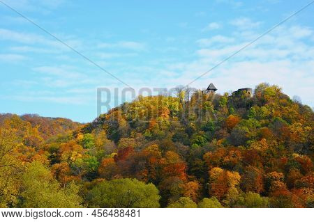 The Mountains Are Covered With Autumn Wood On The Background Of The Blue Sky. On The Mountain Stands