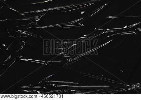 Crumpled Wrinkled Plastic Cellophane. Transparent Plastic Wrap On Black Background. Reflecting Light