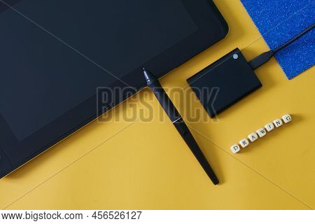 Graphic Tablet With An Interactive Screen And A Stylus On A Yellow-blue Geometric Background Next To