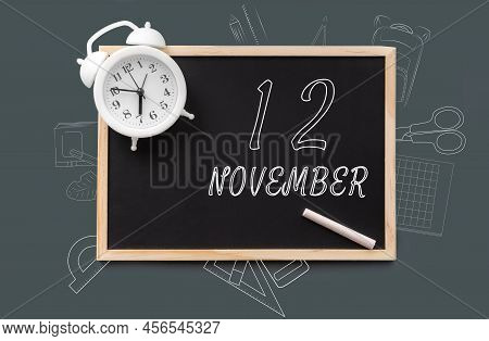 November 12. 12th Day Of Month, Calendar Date. Blackboard With Piece Of Chalk And White Alarm Clock 