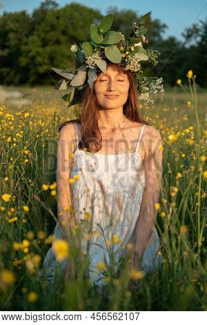 Woman With A Flower Wreath On Her Head Sits In A Field And Enjoys The Sun.