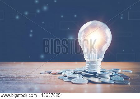 Saving Energy And Money Concept. Idea For Save Or Investment. Lightbulb On And Coins Stacking On Des