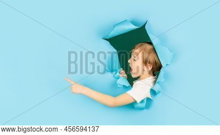 Boy In Blue Paper Hole Pointing With Finger Aside. Screams Boy Looking Through Hole In Paper Wall. S