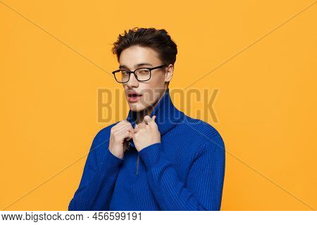 An Attractive Young Man Stands On An Orange Background In A Blue Zip-up Jacket And Black Eyeglasses 