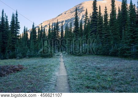 Morning Sun Lights Up A Peak While Meadows Are Still In A Shadow. Cold Sunny Morning In Glacier Nati