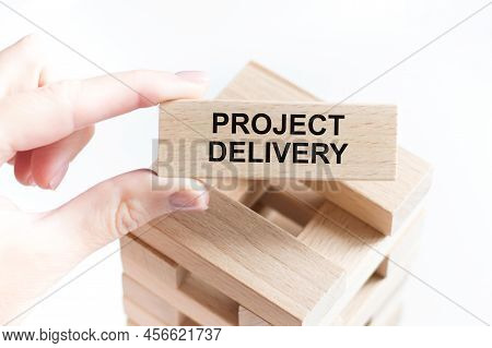 Project Delivery Text On A Wooden Bar In The Hands Of A Businessman Against The Background Of A Towe
