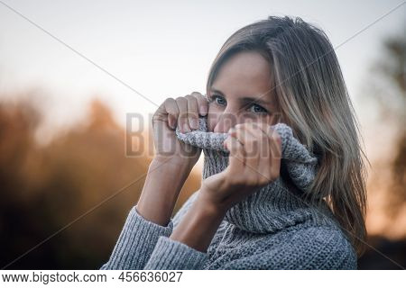 Close-up Of Blonde Woman Face Standing In Forest, Looking Away Smiling And Pulling Sweater Collar Ov