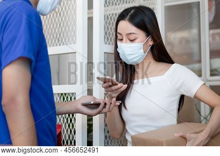 Young Asian Woman,client Wearing Face Mask, Using Mobile Scan Accept A Delivery Of Baggage, Cardboar
