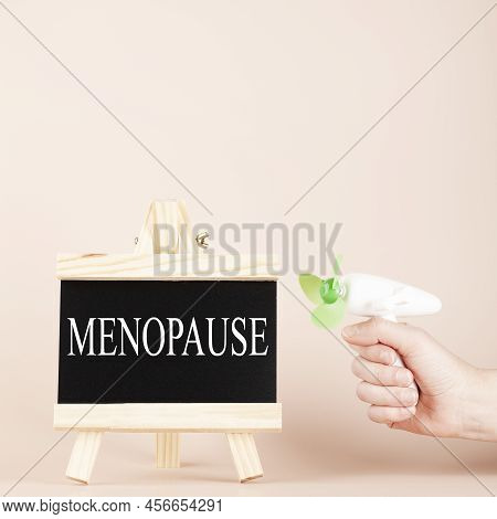 Menopause Word Written On Black Board And Hand Holding Fan On Beige Background. Women Health And Mid