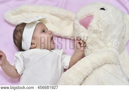 White Dreesed Newborn Baby Looking At Her White Bunny Toy. Cute Mixed Race Baby Girl
