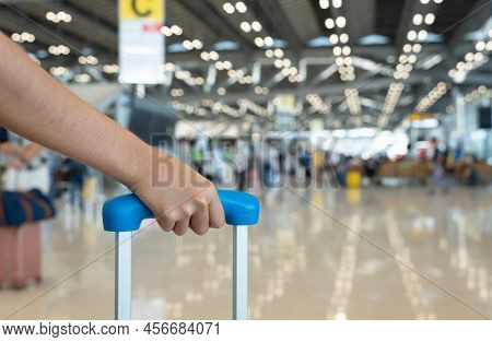 Woman Traveler Hand Holding Luggage With Blurred Passengers Walking In Airport Terminal. Travel Holi