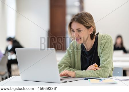 Smiling Middle-aged Woman Studying Online On Laptop Computer While Sitting In Classroom, Doing Secon