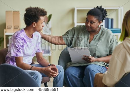 African Young Psychologist Talking To Teenage Boy During Therapy Session At Classroom