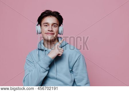 Horizontal Photo On A Pink Background Of A Funny Young Man In A Light Blue Hoodie, Pointing With His