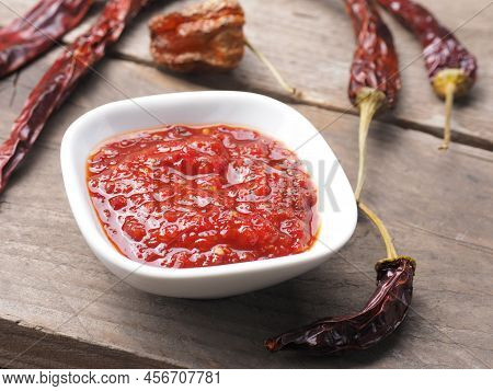 Very Spicy Chili Sauce In A White Bowl On A Rustic Wooden Kitchen Table, Dried Chili Peppers As Deco