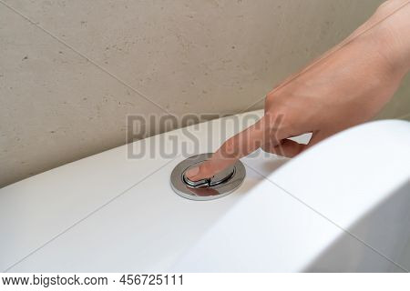Woman's Hand Presses A Button On A White Toilet To Flush