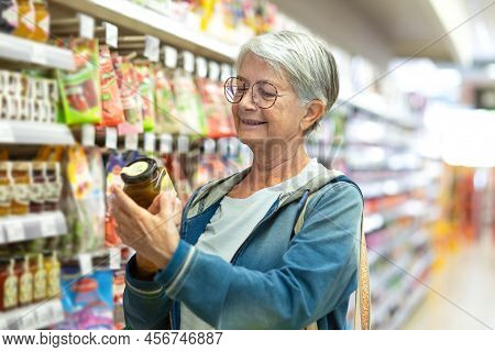 Portrait Smiling Senior Woman Making Purchases In The Supermarket Selecting Some Jam. Caucasian Elde