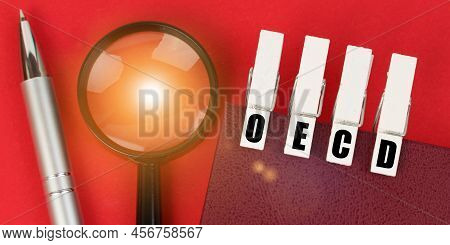 Business Concept. On The Red Surface There Is A Magnifying Glass, A Notepad And Clothespins With The
