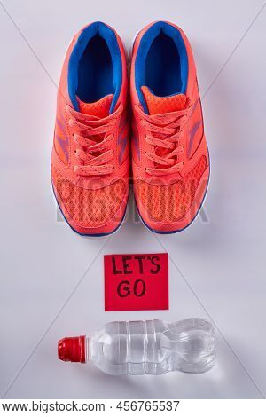Red Shoes With Bottle Of Water On White Background. Lets Go Inscription On Sticker Note.