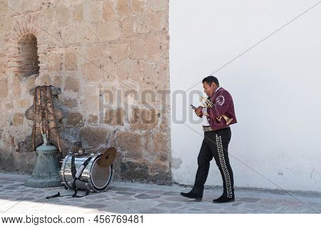 Tlacolula, Oaxaca, Mexico- May 23, 2022: Trumpeter, Member Of Mariachi Checking His Cell Phone Outsi