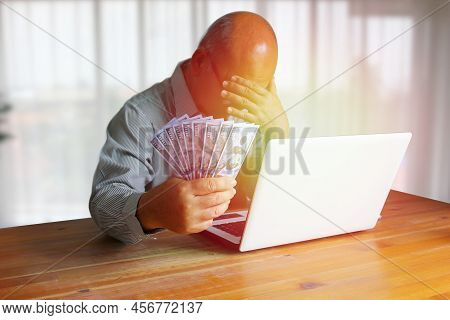 Senior Finansier Holding Dollar In Hand Working With Laptop In Sad Moment