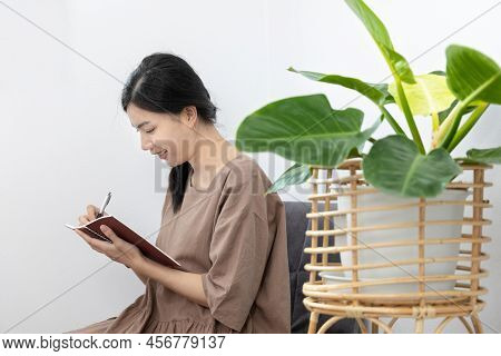 Asian woman sits in her living room writing a diary or notebook on the carpet, Weekends or holidays 