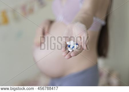 Beautiful Young Pregnant Woman Holds Vitamins Pills Tablets In Her Hand Selective Focus Copy Space. 